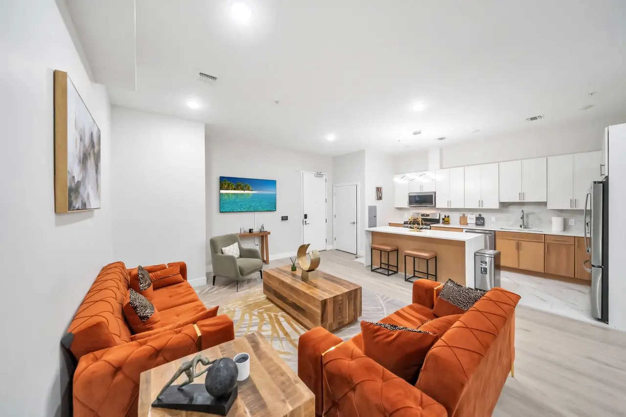 Living room with orange velvet sofas, wooden coffee table and open kitchen behind