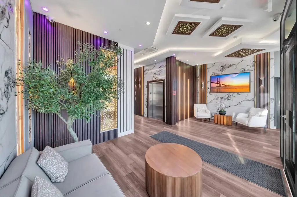 Building lobby with grey sofa, round wood table, indoor tree and wall-mounted TV